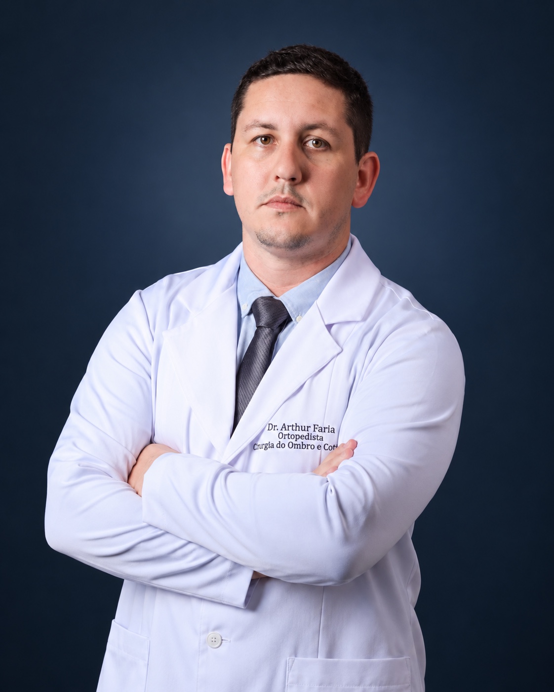 Dr. Arthur Faria, ortopedista, de jaleco branco e braços cruzados